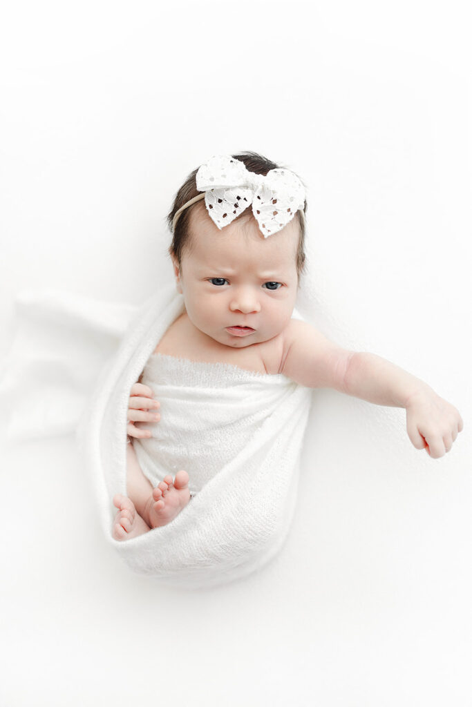 newborn baby girl awake in white wrap with eyelet bow, NYC newborn photographer, Heirloom by Melissa Photography