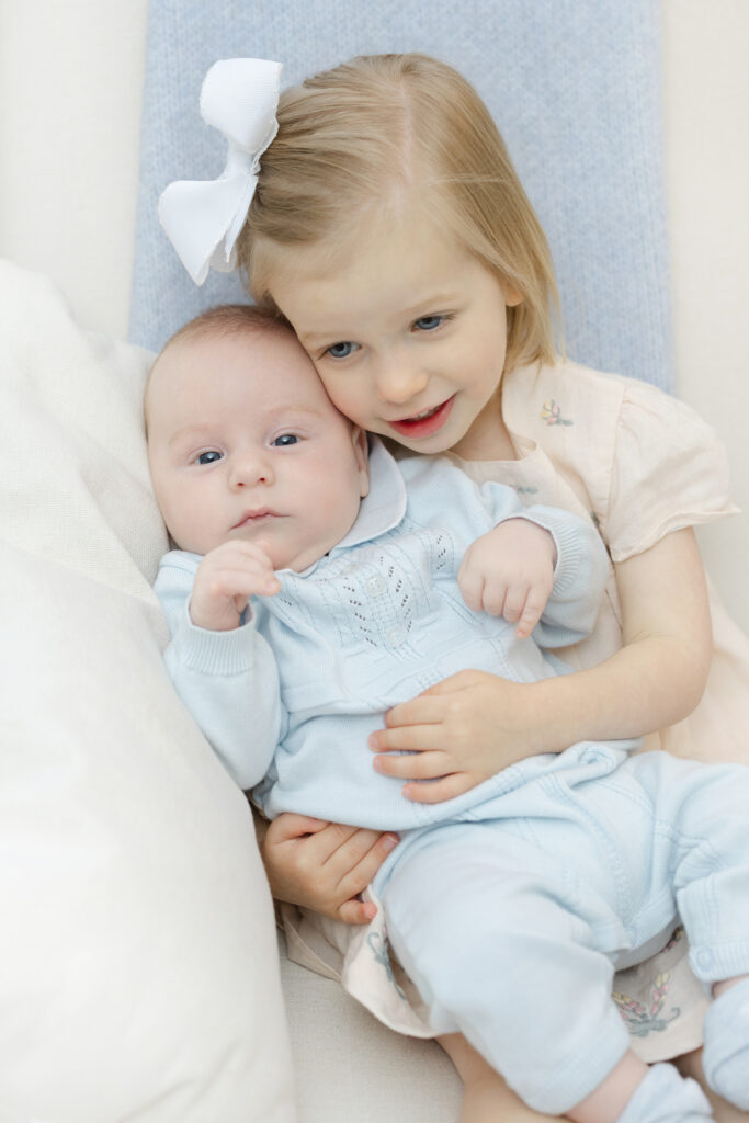 Big sister cuddling newborn baby during lifestyle family photography session in NYC