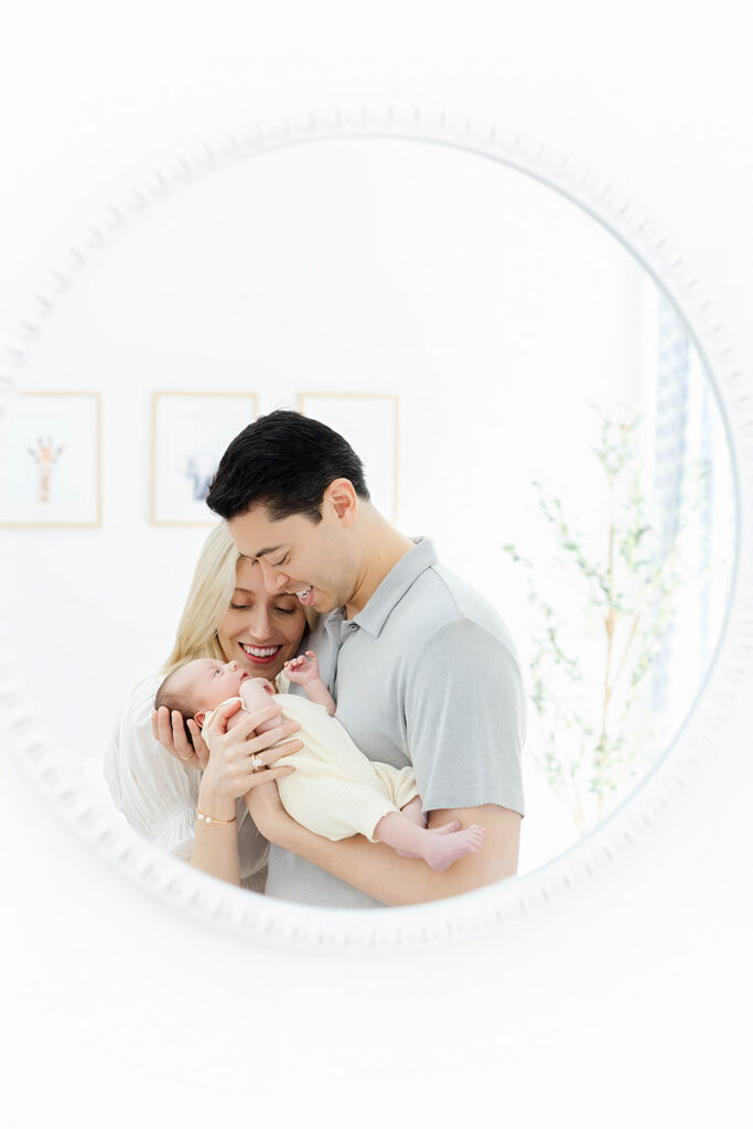 Parents kissing newborn baby in round mirror reflection, NYC baby photographer, Heirloom by Melissa