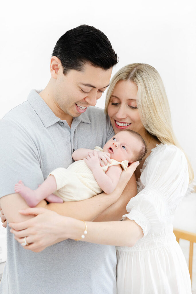 Parents standing in nursery holding newborn baby beside crib, NYC baby photographer, Heirloom by Melissa