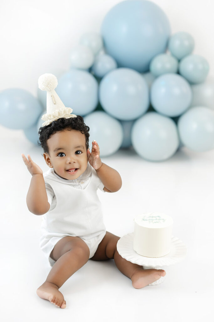  First birthday cake smash NYC, birthday boy in a party hat with a blue balloon garland at Heirloom by Melissa, Manhattan