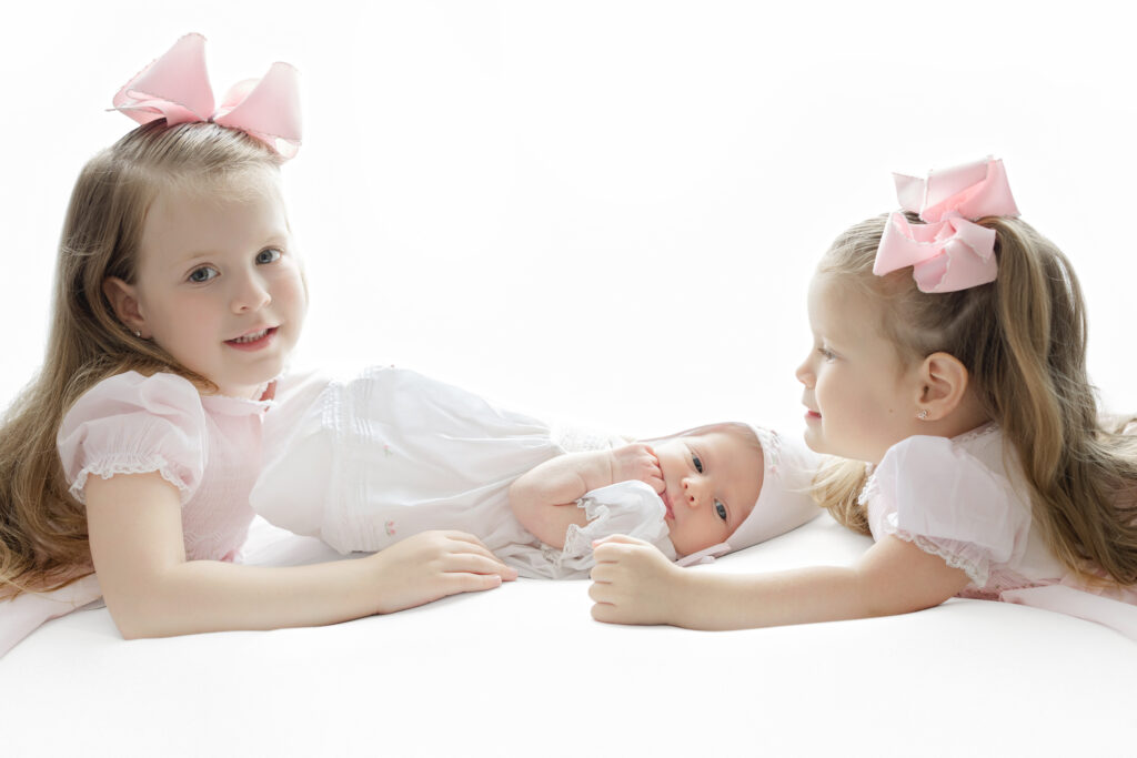  Big sisters holding newborn during in-home session with New York newborn photographer Heirloom by Melissa