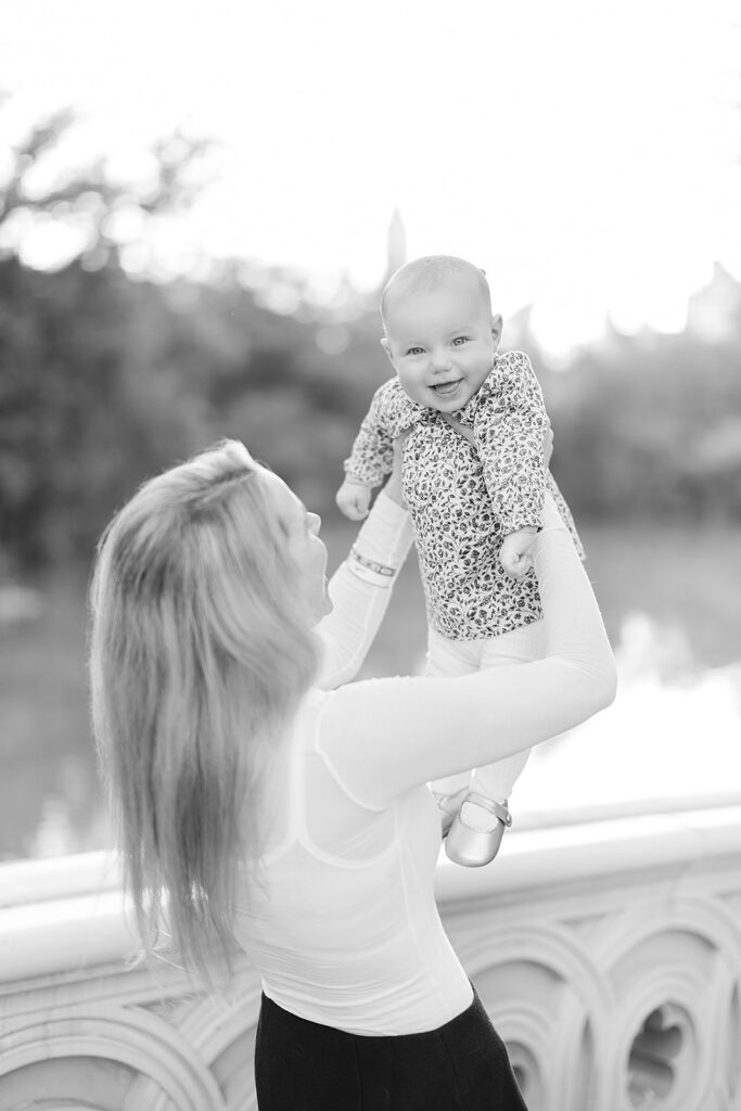 Mother lifting her baby into golden hour light on Bow Bridge in Central Park, NYC family photographer Heirloom by Melissa Photography