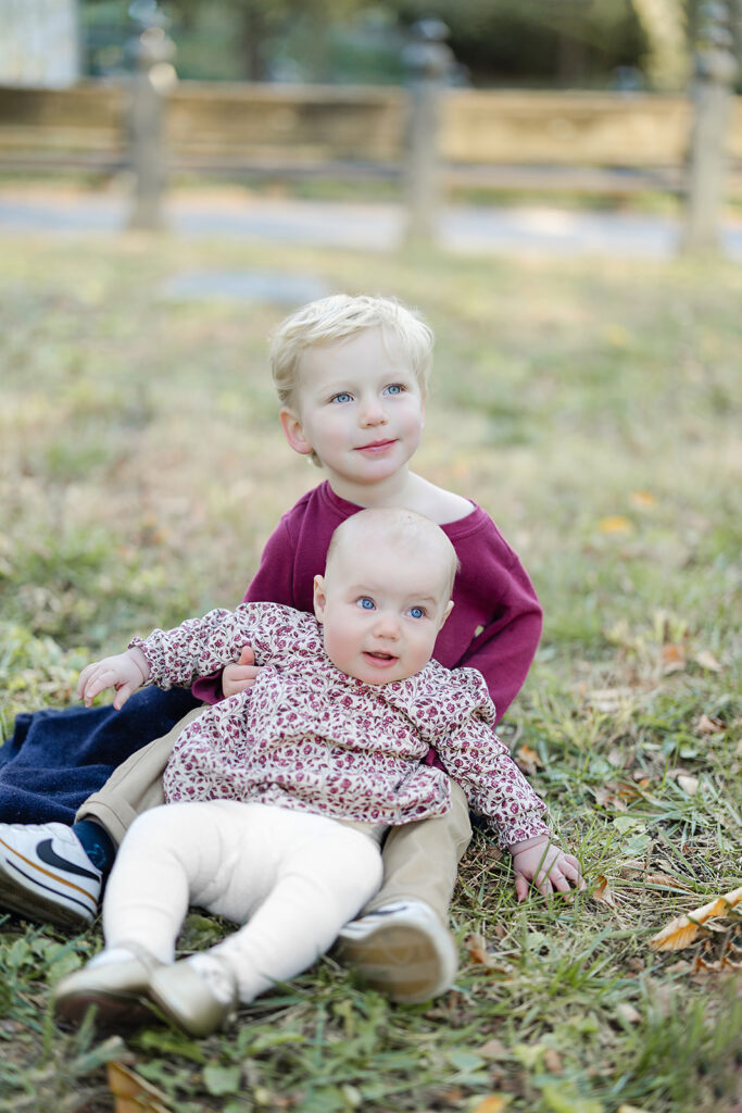 Big brother holding his baby sister in the grass during a fall NYC family photographer session in Central Park, Heirloom by Melissa Photography