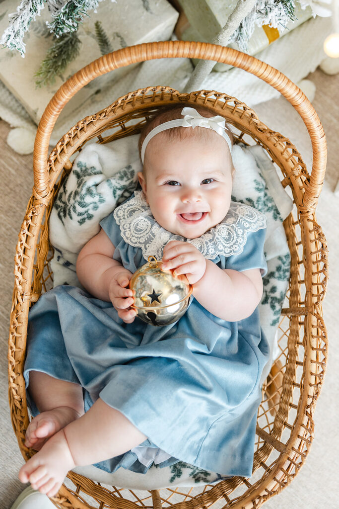 Baby's first holiday photos NYC, baby holding a gold jingle bell in a bassinet at Heirloom by Melissa, Manhattan