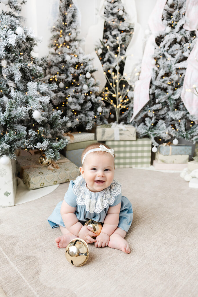 Baby's first holiday photos NYC, baby seated among flocked trees and presents at Heirloom by Melissa's Flatiron studio