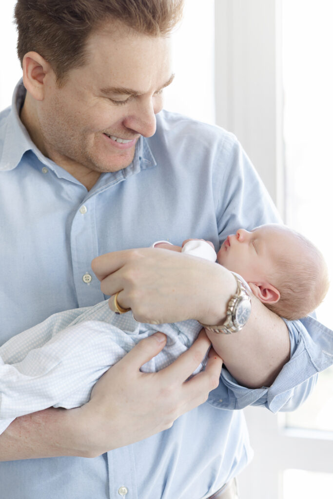 Father holding his newborn son and looking down at him near the window