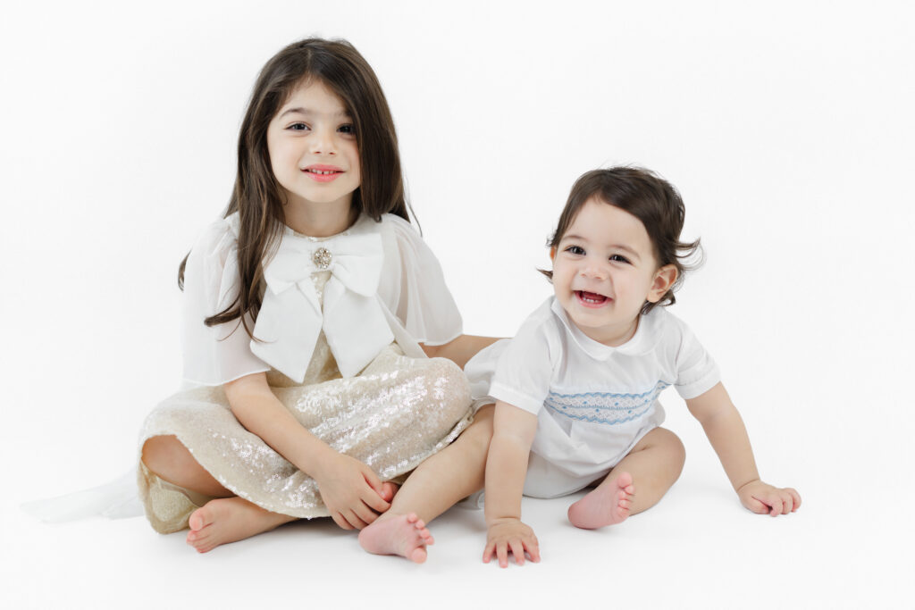 Soren and his older sister smiling together against a white backdrop