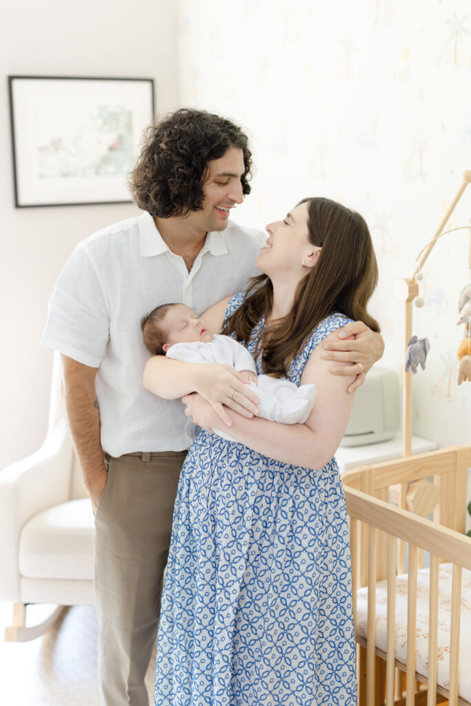 Parents holding their newborn son beside his crib at home