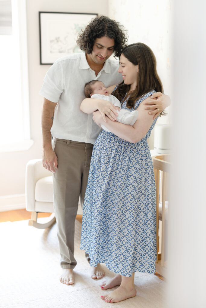 Parents posing with their newborn baby and corgi against a white wall