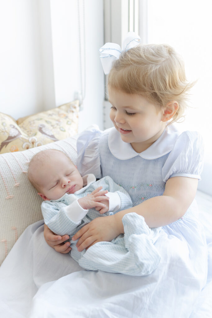 Older sibling looking at the new baby while holding him at home