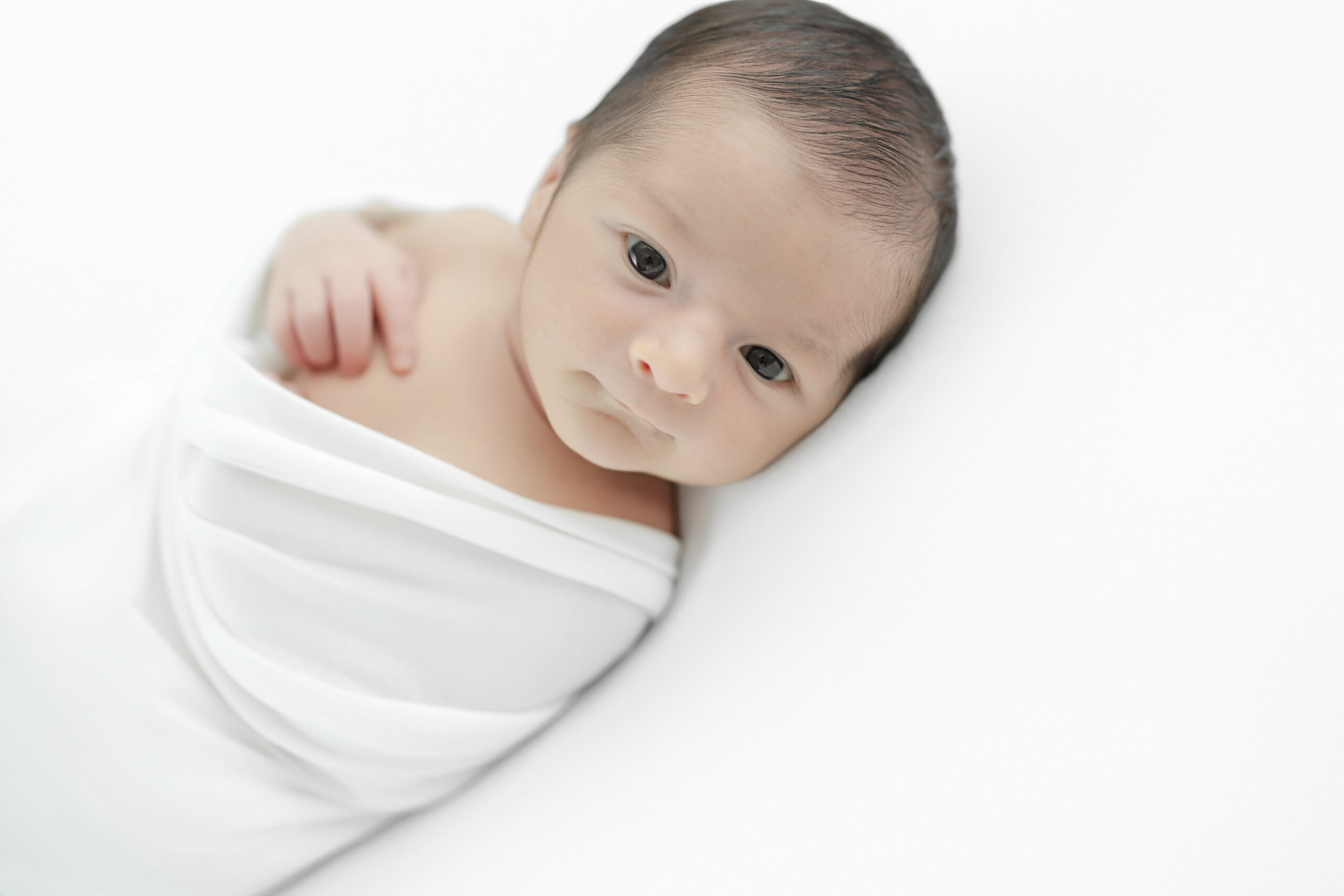 Awake baby boy wrapped in white during a timeless NYC newborn photography session