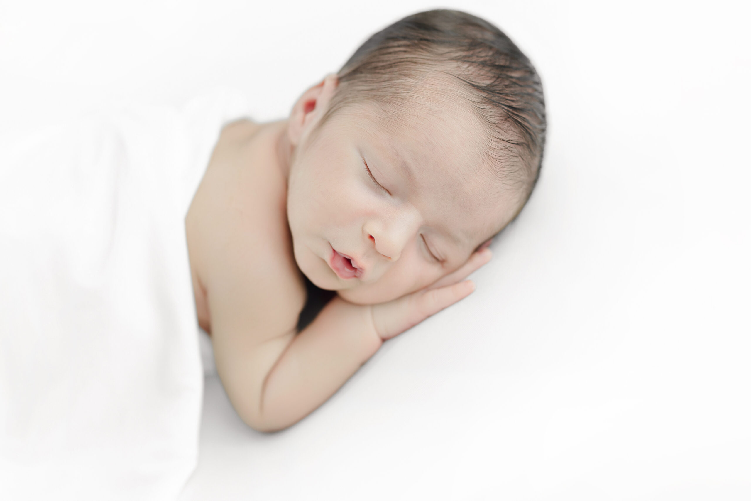Close-up of a sleeping newborn resting his face on his tiny hands