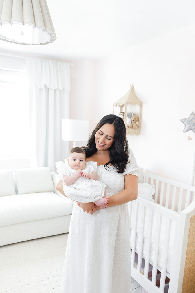 Mother holding her three-month-old daughter beside the crib in their Manhattan home