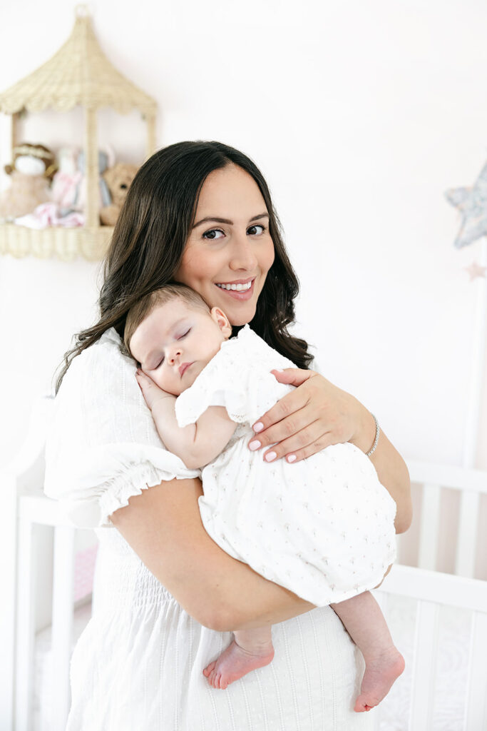 Mother smiling while holding her baby girl in a light-filled nursery