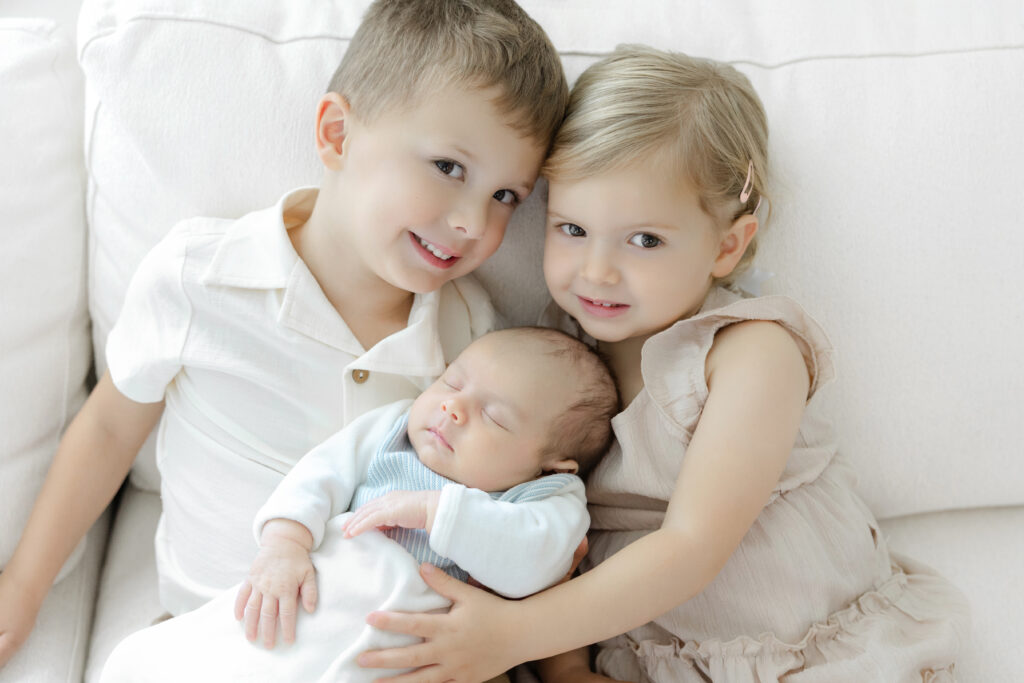 Brother and sister cuddling their newborn sibling at home