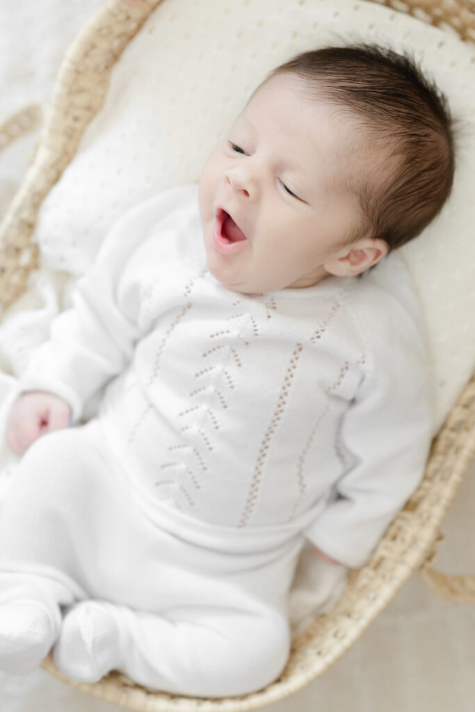 Newborn baby in a white outfit resting in a woven basket