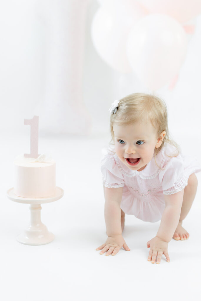 Eleanor crawling beside her pink cake at her NYC first birthday session