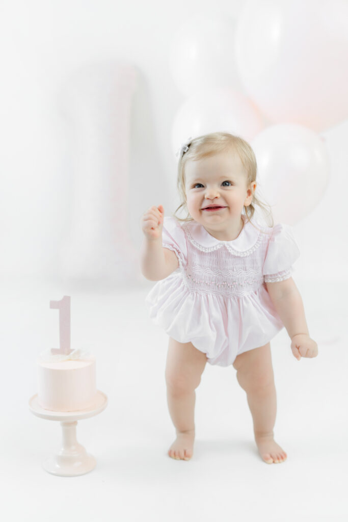 Eleanor standing in a pale pink outfit beside her birthday cake