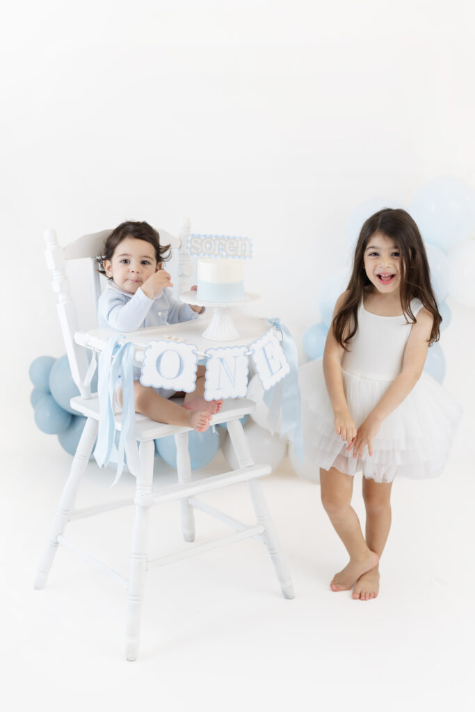 Soren in his birthday high chair with his older sister standing nearby