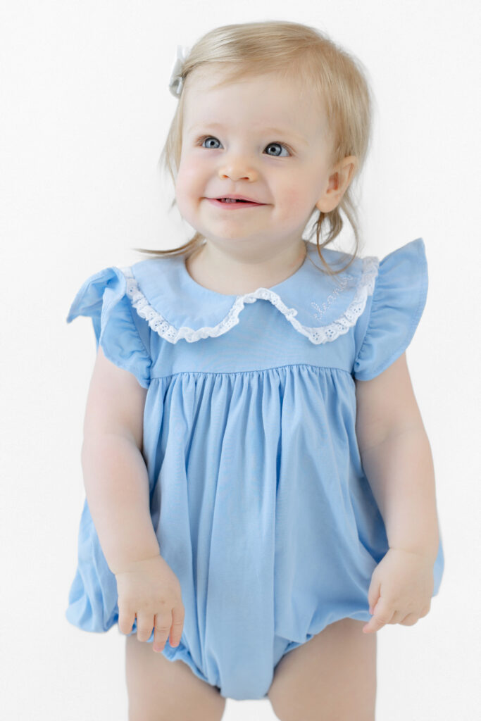 Eleanor smiling in a blue outfit during her first birthday studio portraits
