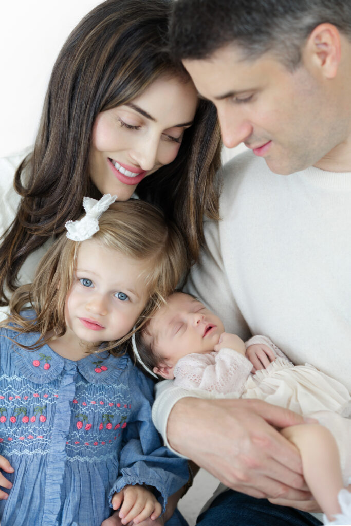 Parents leaning close to their newborn and older daughter during family portraits