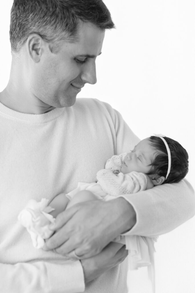 Black and white portrait of a father holding his sleeping newborn baby
