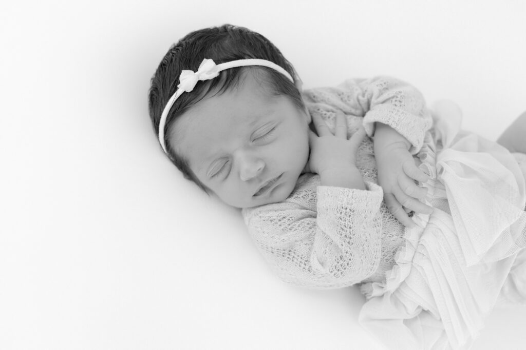 Black and white studio portrait of a sleeping newborn wearing a small bow
