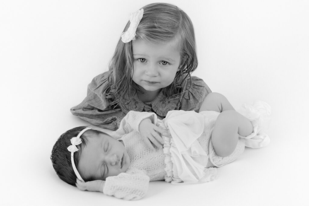 Older sister sitting beside the newborn baby during their NYC studio session