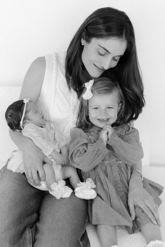 Mother holding her newborn baby while her older daughter sits beside them