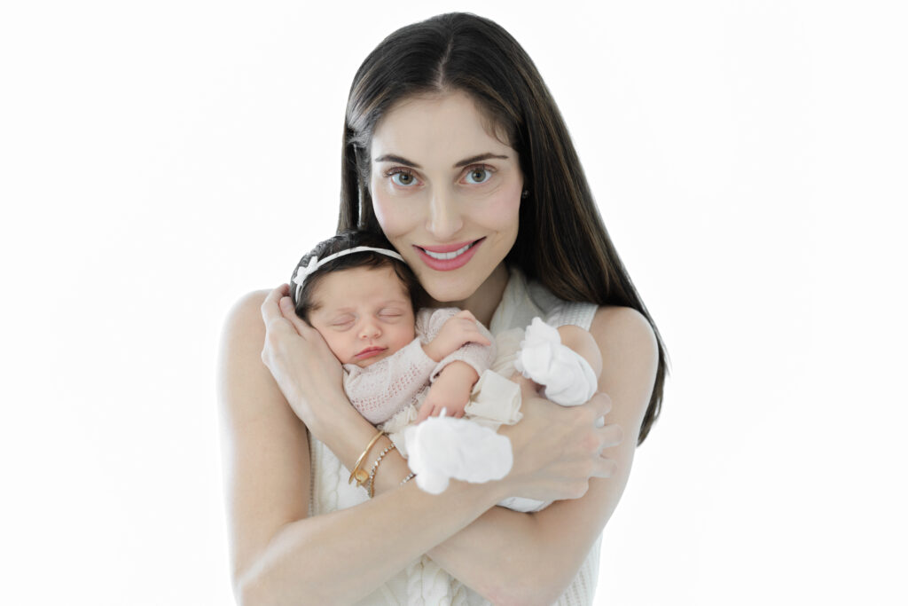 Mother holding her newborn daughter close against a white studio backdrop