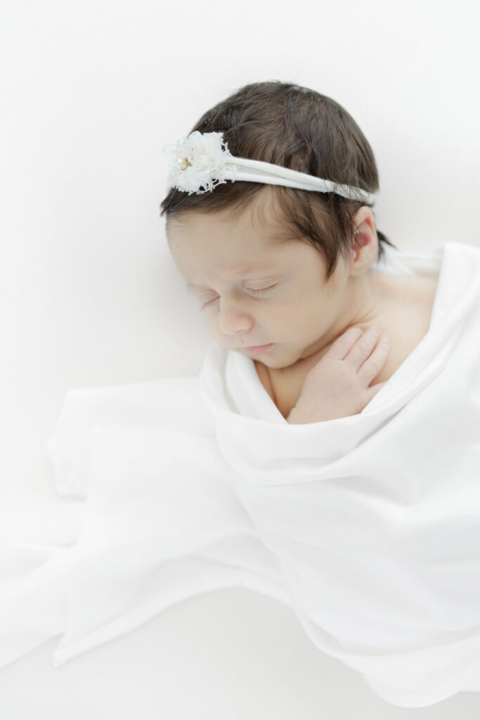 Sleeping newborn baby in a white swaddle with a white bow