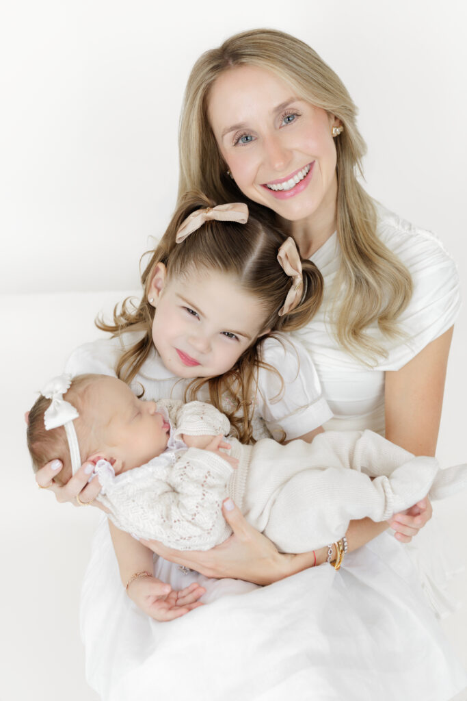 Mother holding her newborn while her older daughter leans in beside them