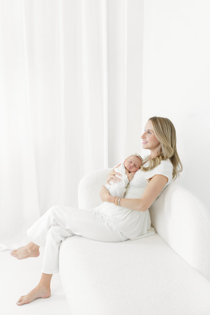 Mother seated on a white sofa holding her sleeping newborn