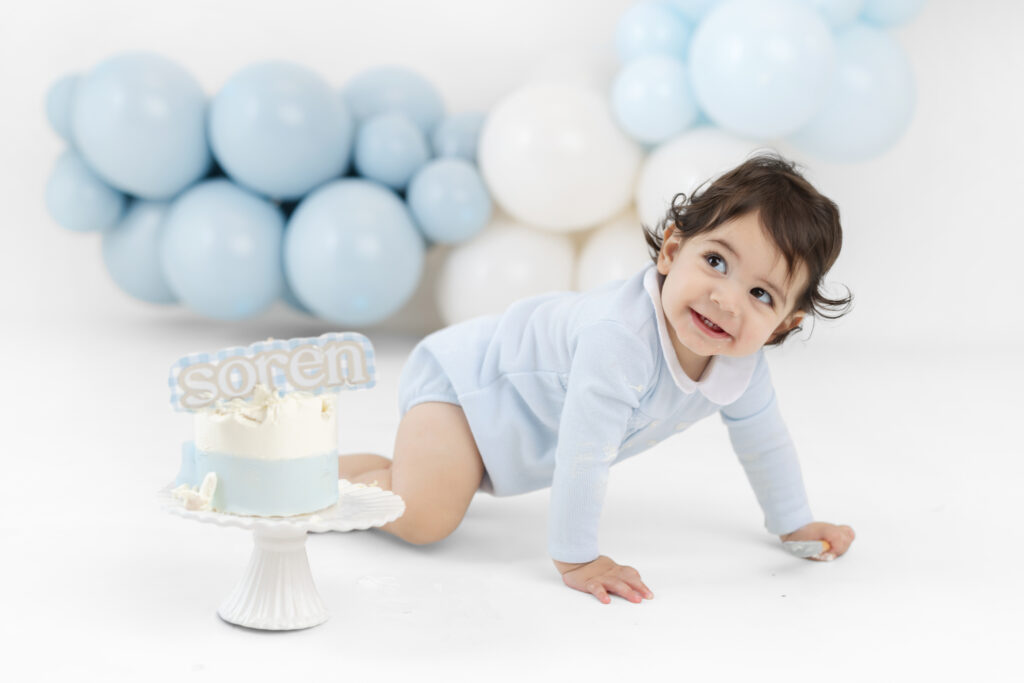 Soren sitting in front of soft blue balloons for his first birthday portraits