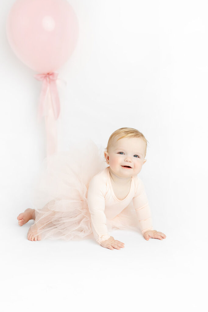 NYC first birthday portraits of a baby girl in a pale pink dress beside her cake